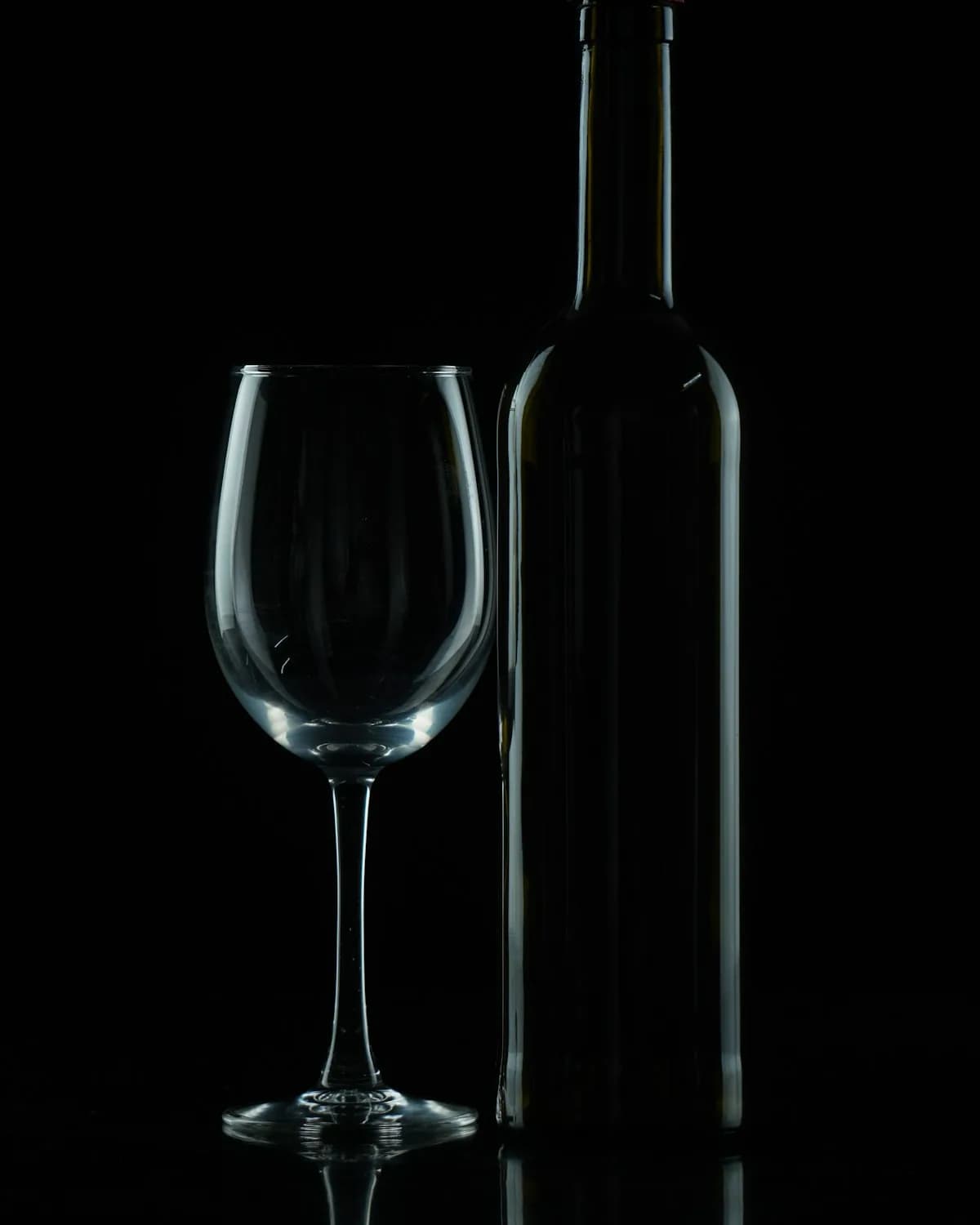 Weinglas und Flasche im Halbdunkel, sinnbildlich für unsere Weinauswahl